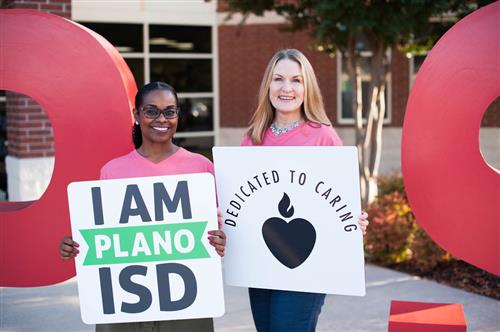 Patricia Hempstead and Deni Bleggi holding signs that say "I am plano ISD" and "Dedicated to Caring" 
